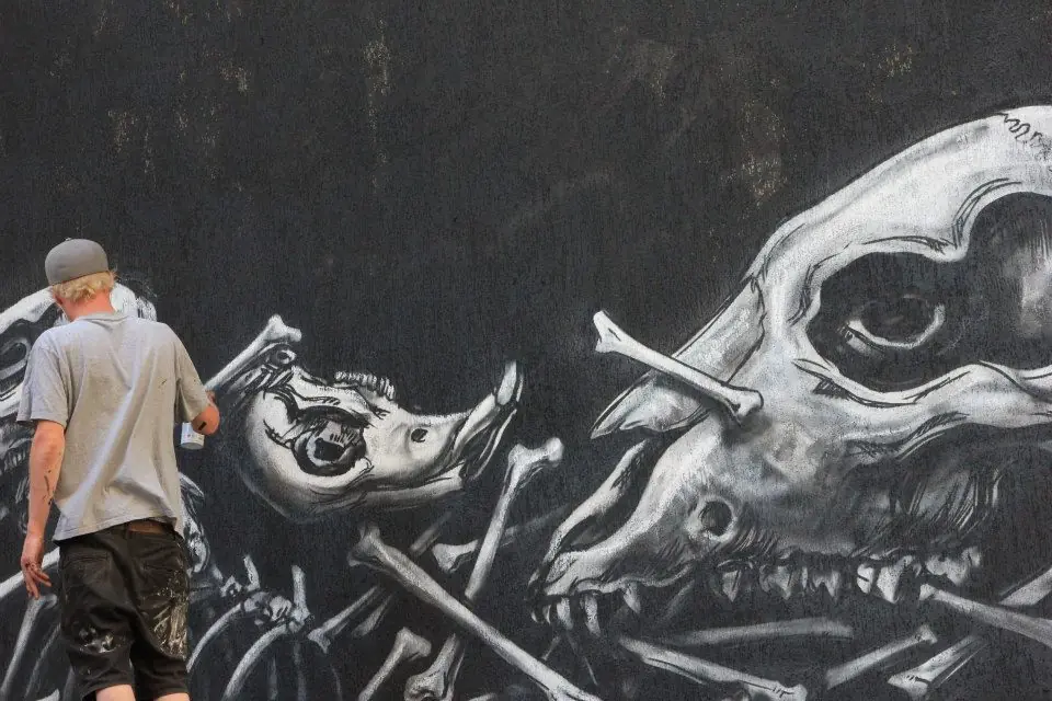 A painter works close to the mural’s dark background and animal outlines