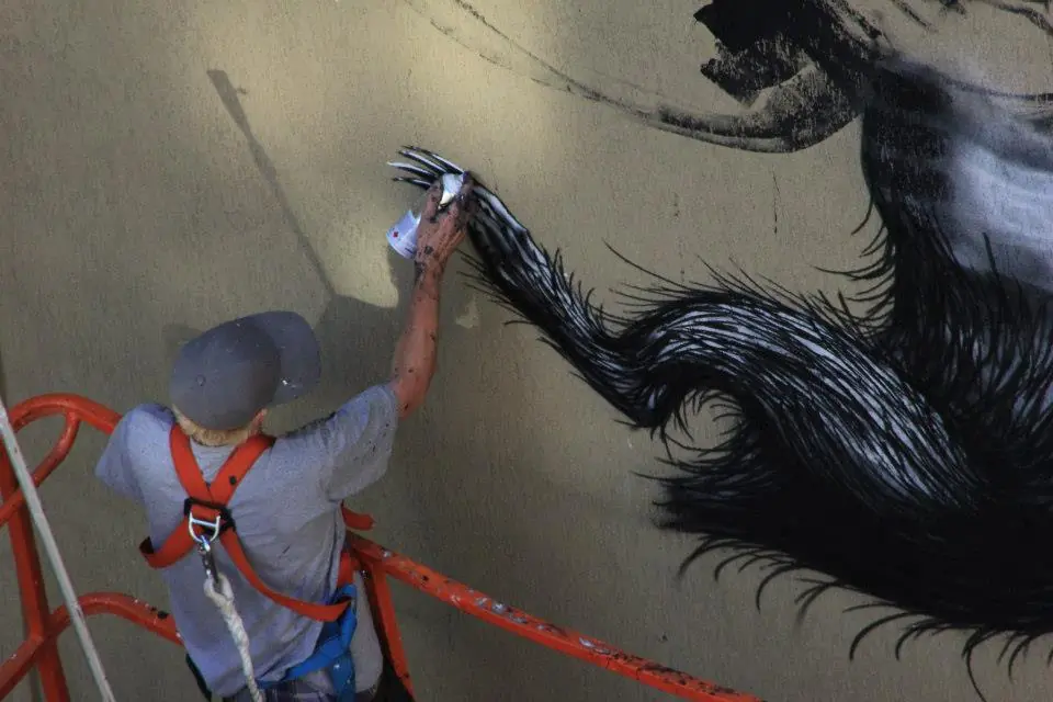 A painter in a lift adds detail to the large animal mural