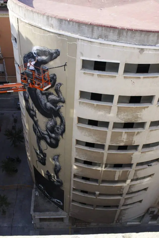 Wide view of the mural being painted from a lift beside the curved building